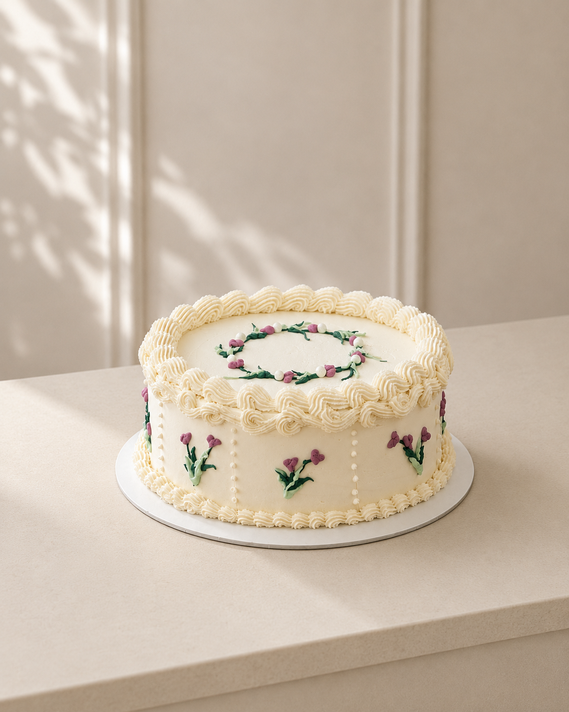 Minella Patisserie vintage-style ivory cake with piped buttercream, green vine details, and small pink flowers.